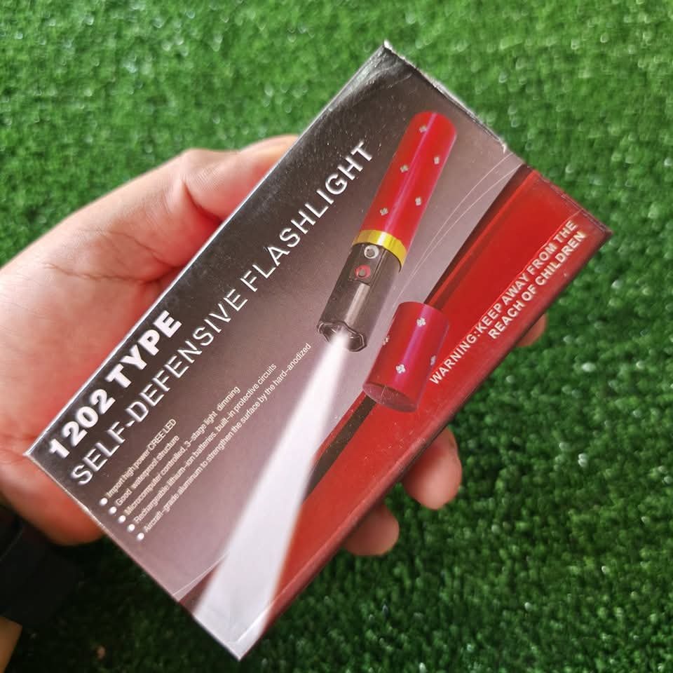 1202 Type Self-Defensive Flashlight retail packaging box showing a red lipstick-shaped hidden stun gun torch with a bright LED light beam